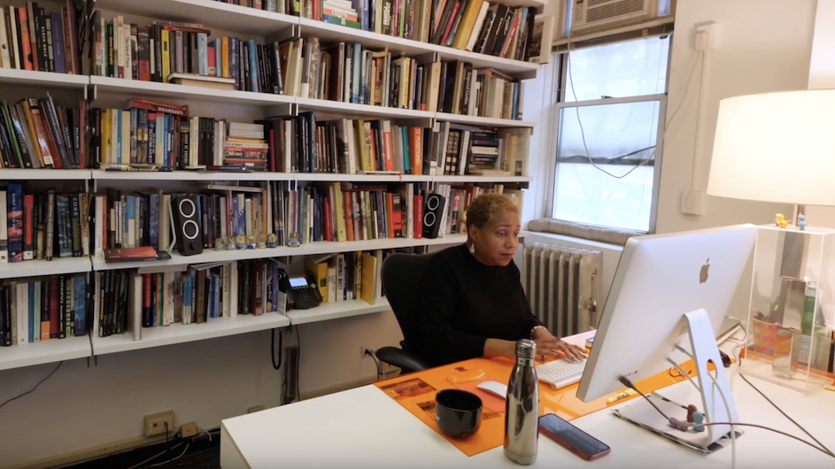 Woman sitting at her desk on her computer with shelves of books behind her