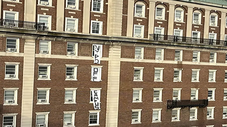 Hamilton Hall dorm room windows reveal white flags with dark letteirng spellling out NYPD Off Campus