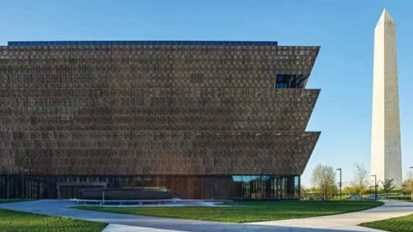 Photo of the front facade of the National Museum of African American History and Culture on a bright, sunny day with the Washington Monument in the background. Photo by Alan Karchmer/NMAAHC.  