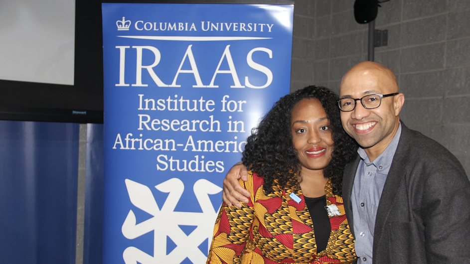 A woman and a man in a friendly embrace standing next to a standing banner with the words Columbia University and IRAAS