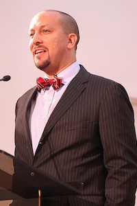 Man speaking at a podium wearing a suit with a bowtie